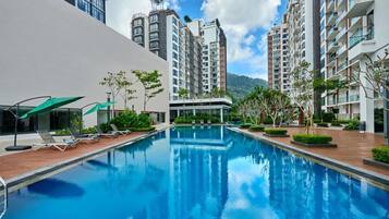 A swimming pool surrounded by modern apartment buildings with balconies, a clear sky, and some greenery.