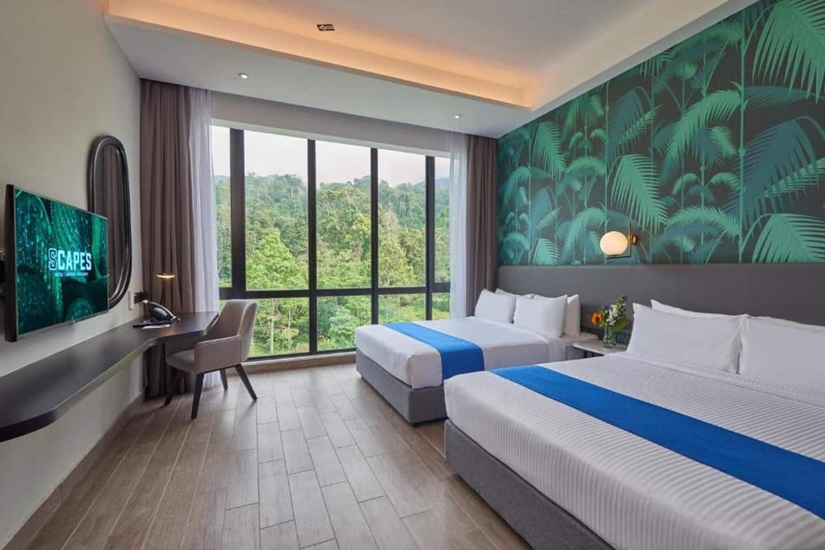 A hotel room with two beds, a desk, a TV, and a large window with a view of the forest.