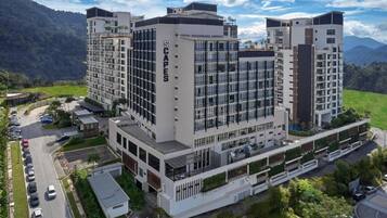 A modern multi-story hotel with a central courtyard, surrounded by lush greenery and mountains in the background.