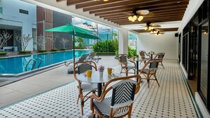 A poolside area with a tiled floor, wicker chairs, a table with yellow cups, and a ceiling with wooden beams and hanging lights. - Scapes Hotel (Genting Highlands)