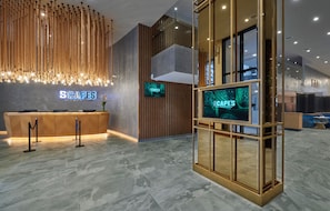 A hotel reception area with a modern design, featuring a reception desk, a digital screen displaying the hotel name, and a decorative wooden wall. - Scapes Hotel (Genting Highlands)