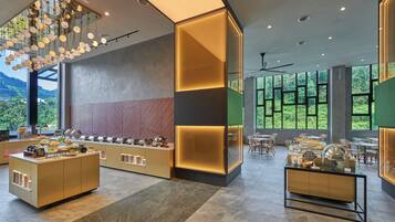 A modern hotel lobby with a buffet area, large windows offering a view of greenery, and contemporary lighting fixtures.