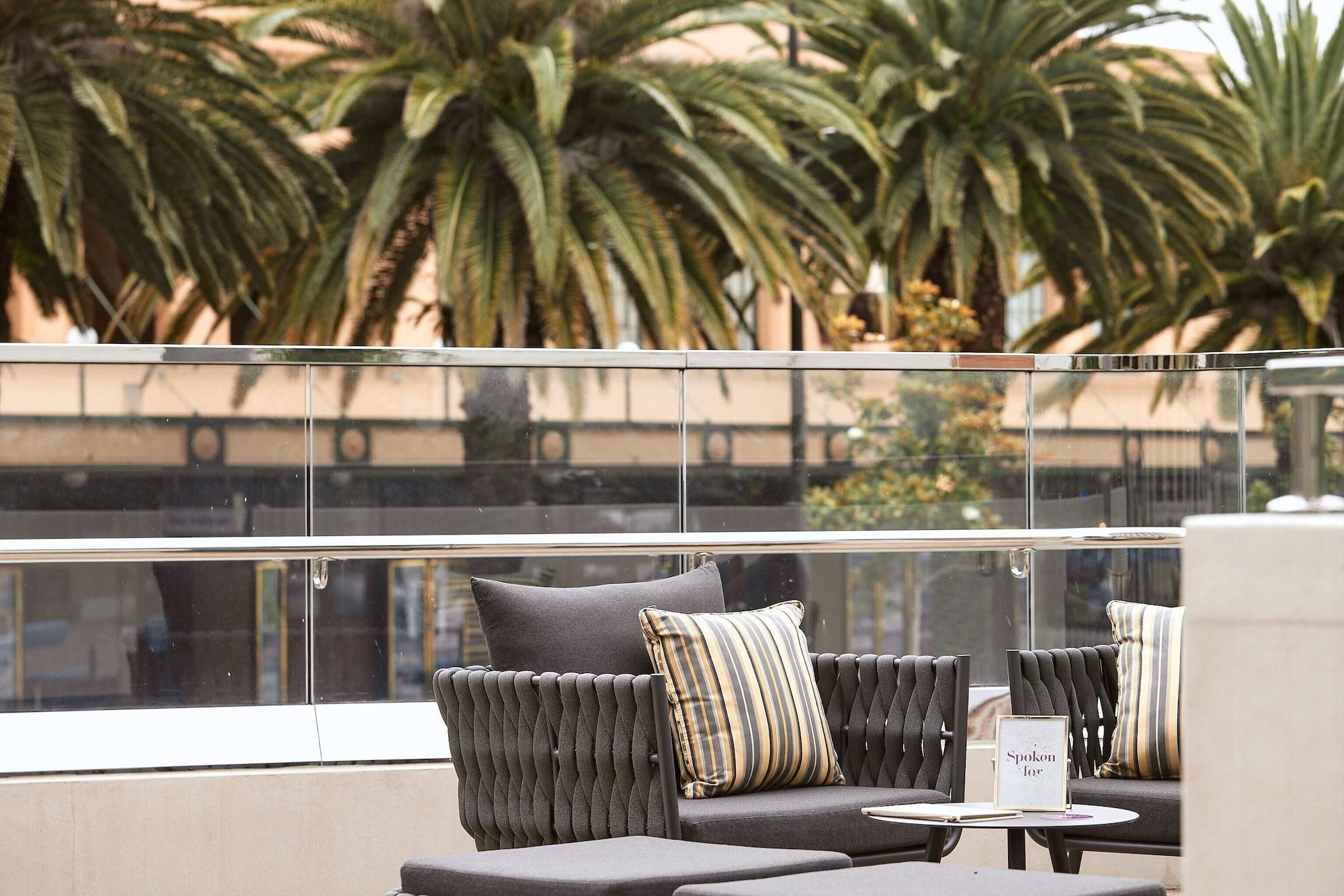 A balcony with a sofa and chairs, a small table, and a view of palm trees.