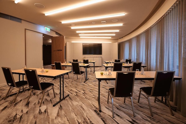 A conference room with multiple tables and chairs, a large screen, and a view of the city through large windows. - Crystalbrook Kingsley (Newcastle)