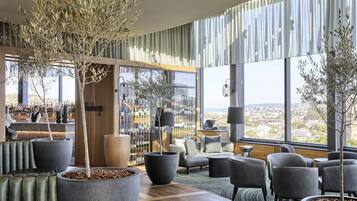 A modern lounge area with large windows, seating, and a bar with visible bottles.