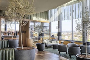 Un espace lounge moderne doté de grandes fenêtres, de sièges confortables et d’un bar où les bouteilles sont exposées.