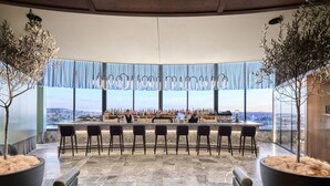 Eine Bar mit einer langen Theke, mehreren Barhocker und Blick auf die Skyline der Stadt.