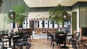 Un restaurante moderno con varias mesas y sillas, una zona de bar central y lámparas colgantes.