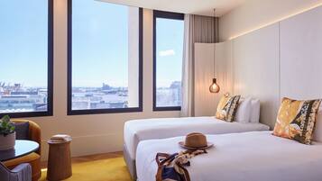 A hotel room with two beds, a view of the city, a small table with a plant, and a hanging light fixture.