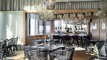 A modern restaurant with a bar area, large windows, and black and white striped chairs.