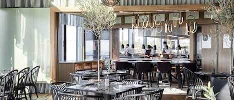 A modern restaurant with a bar area, large windows, and black and white striped chairs.