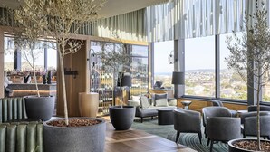 Ein stilvoller Lounge-Bereich mit großen Fenstern, Sitzgelegenheiten und einer Bar mit sichtbaren Flaschen.