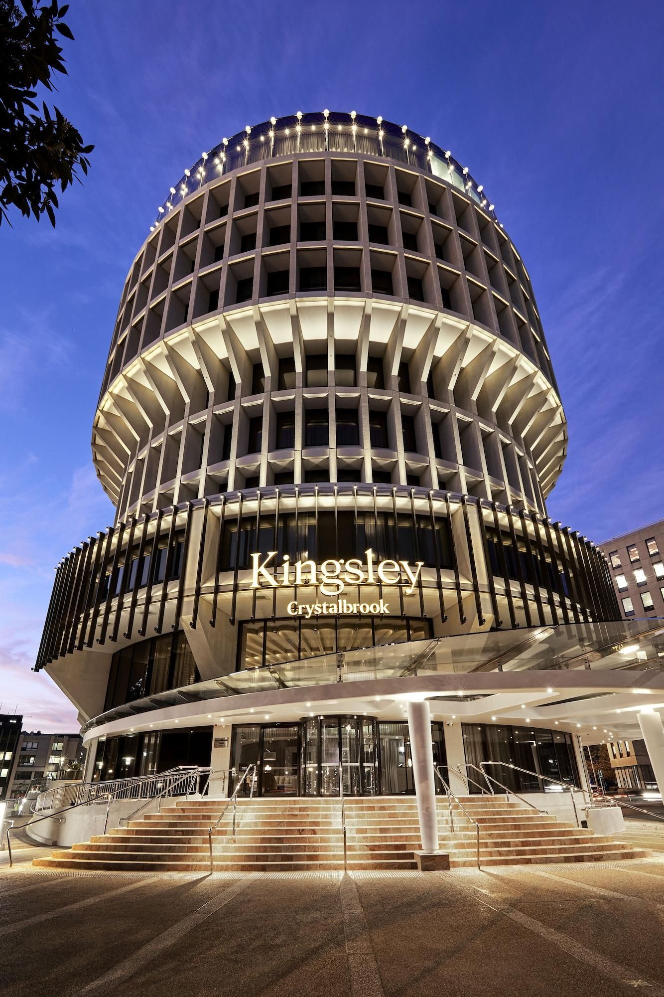 A modern hotel with a circular facade, a prominent Kingsley Crystalbrook sign, and a glass entrance.