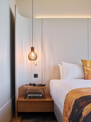 A modern hotel room with a neatly made bed, a bedside table with a lamp, and a flat-screen TV mounted on the wall. - Crystalbrook Kingsley (Newcastle)