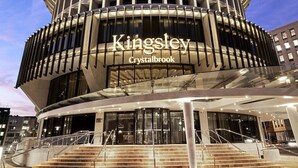 Ein modernes Hotel mit einer kreisförmigen Fassade, einem markanten Kingsley Crystalbrook Schild und einem Glastür-Eingang.