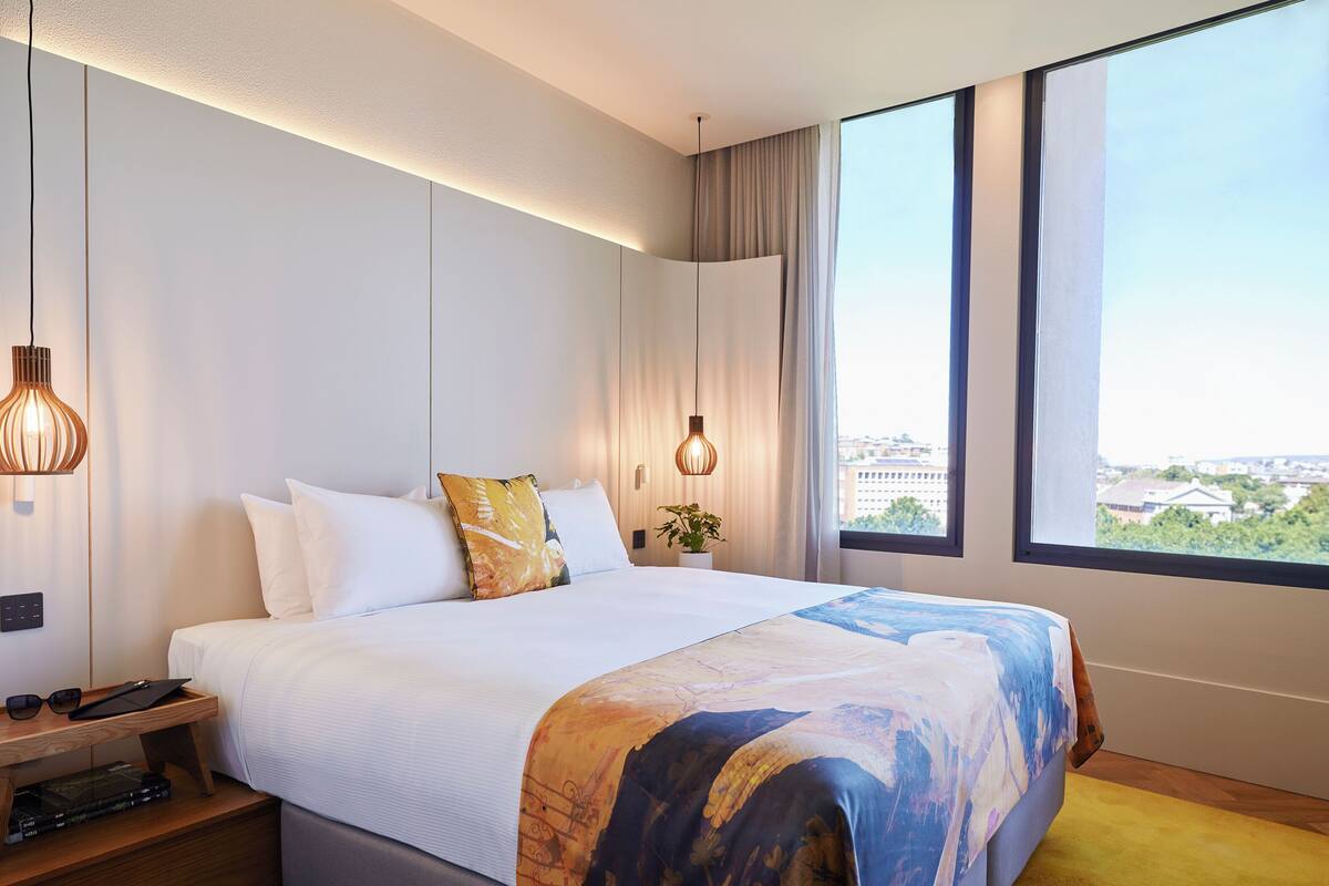 Una camera d'albergo moderna con un letto grande, comodini, vista sulla città e un'ampia finestra.
