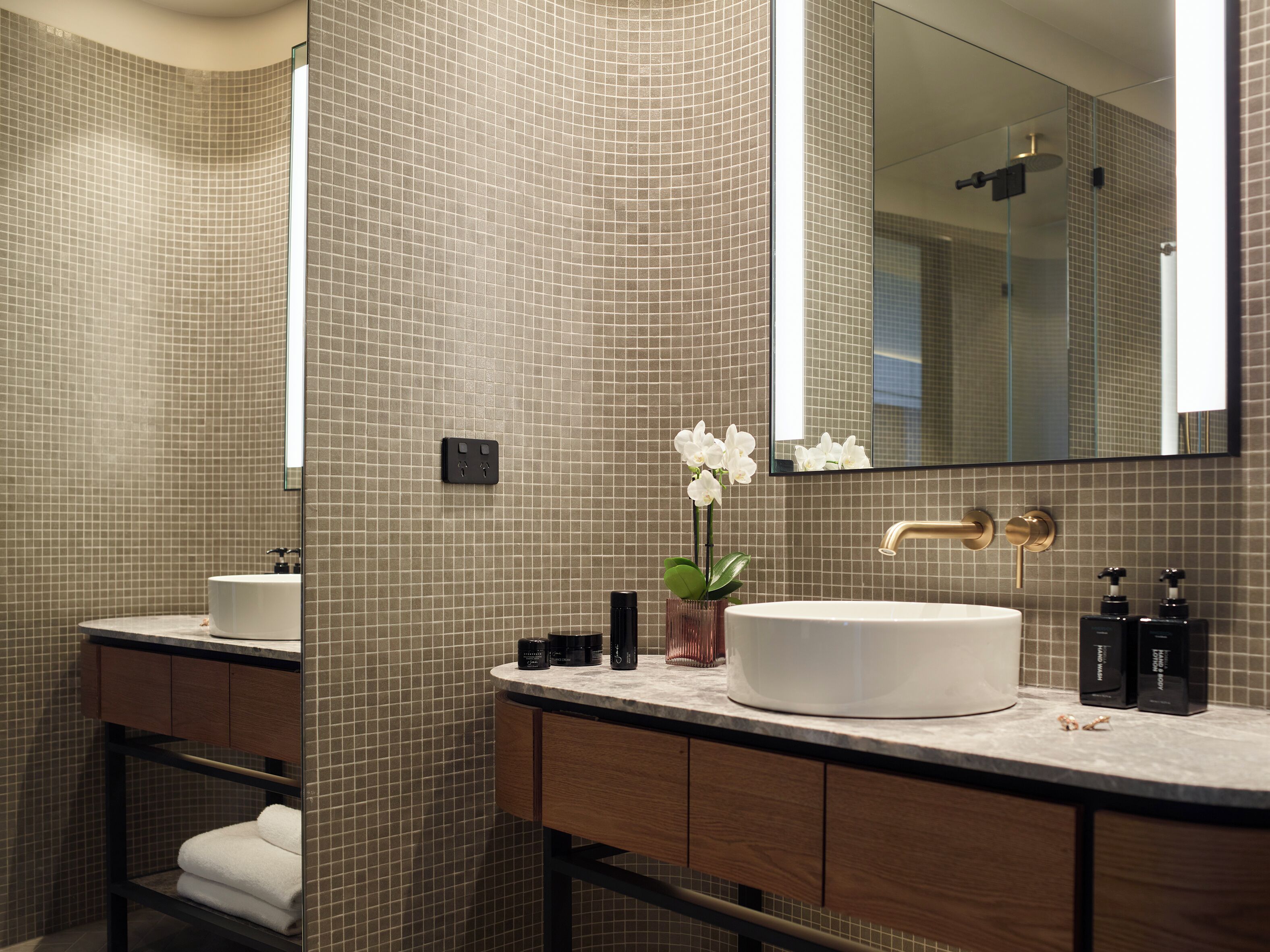 A modern bathroom with a large mirror, two sinks, and a vanity with a towel rack.
