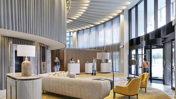 A modern lobby with a large bed, seating area, reception desk, and large windows.