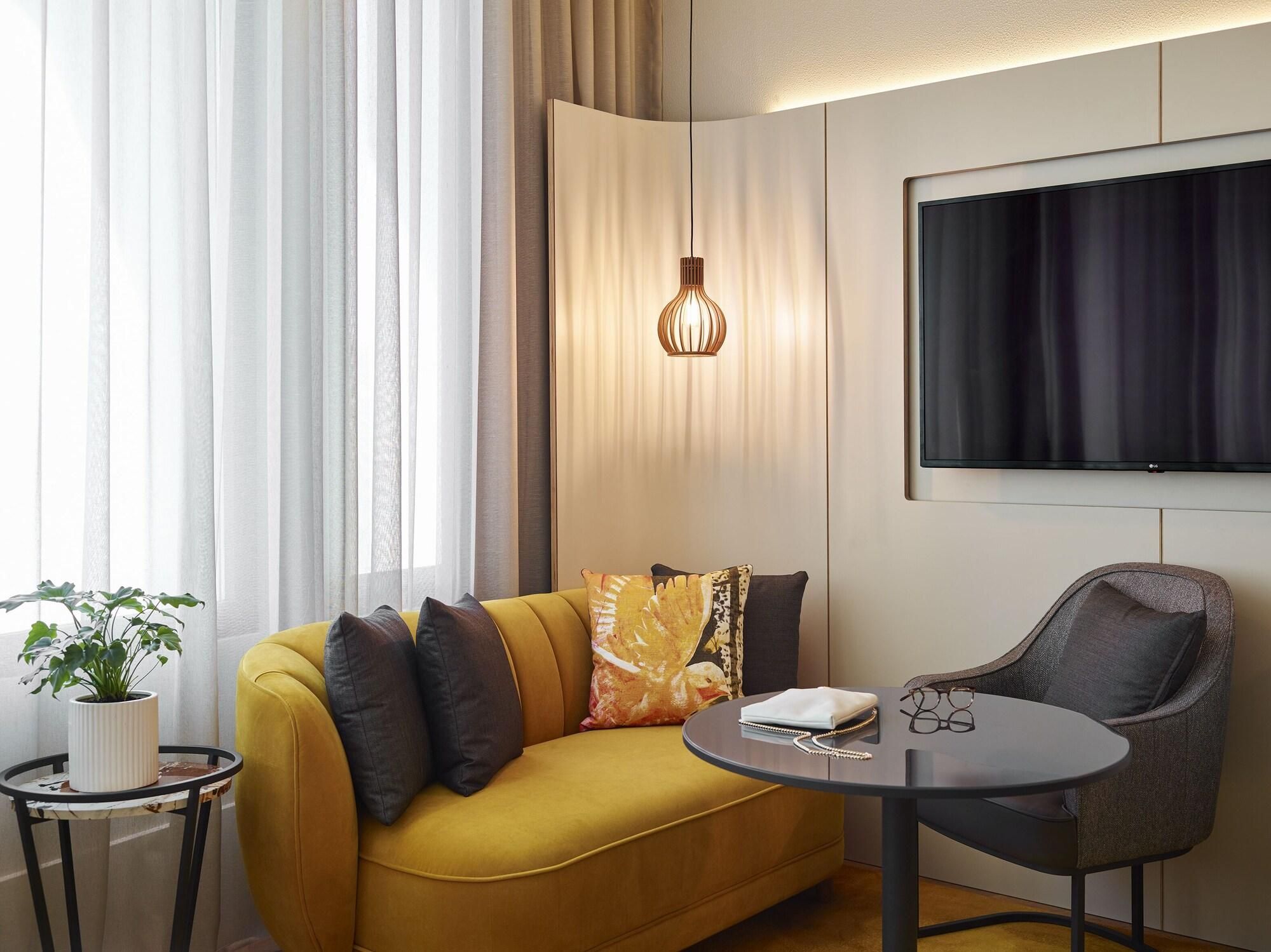 A modern living room with a sofa, a round table, a TV, and a hanging light fixture.