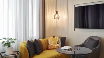 A modern living room with a sofa, a round table, a TV, and a hanging light fixture.