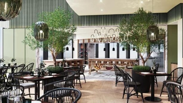 Ein modernes Restaurant mit mehreren Tischen und Stühlen, einer zentralen Bar und hängenden Pendelleuchten.