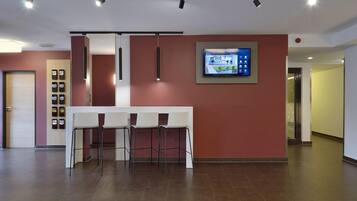 Un moderno vestíbulo de hotel con un mostrador de recepción, zona de estar y una pantalla digital en la pared.