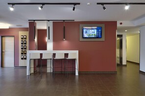 Hall d'ingresso moderna di un hotel con reception, area salotto e display digitale a parete.