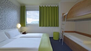 Habitación de hotel con dos camas, una litera, una ventana con cortinas, una lámpara de noche y una pared con texto.