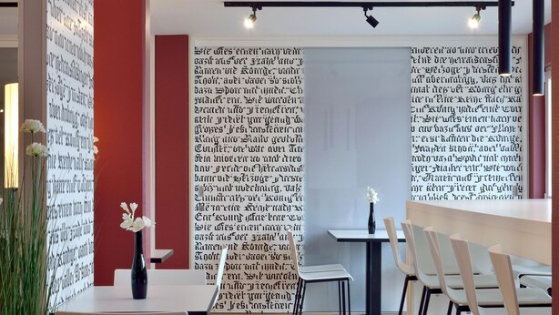 A modern interior with a white table, chairs, and a vase with white flowers. - B&B Hotel München Messe Dornach (Aschheim)