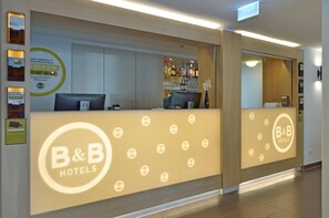 Una reception con il logo B&B Hotels, un computer e un'area bar con diverse bottiglie e bicchieri.