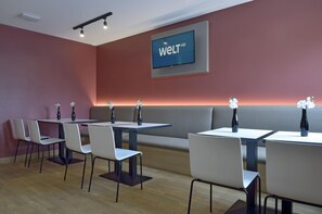 Et moderne spiseområde med borde, stole og en bænk langs væggen. En stor skærm viser 'welt HD'.