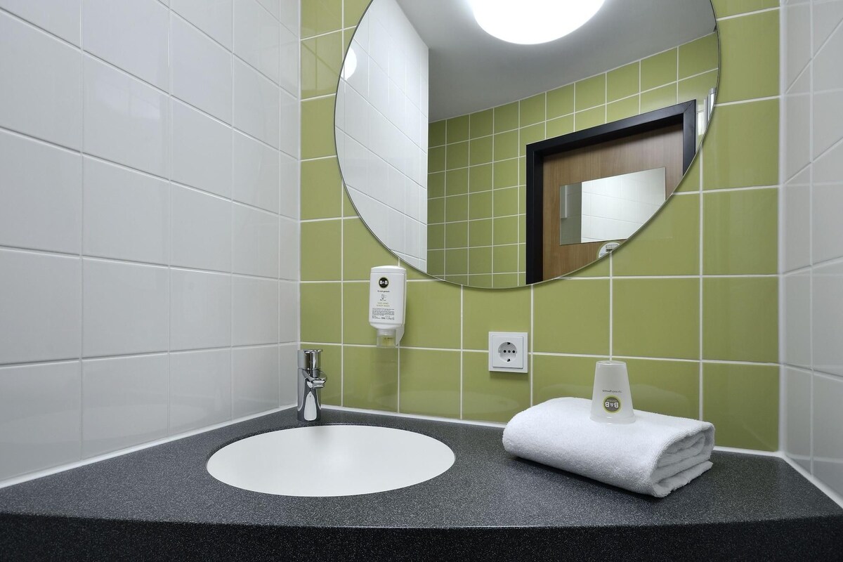 Ein Badezimmer mit einem weißen Waschbecken, einem Spiegel, einem Handtuch und einer Seifenspender.