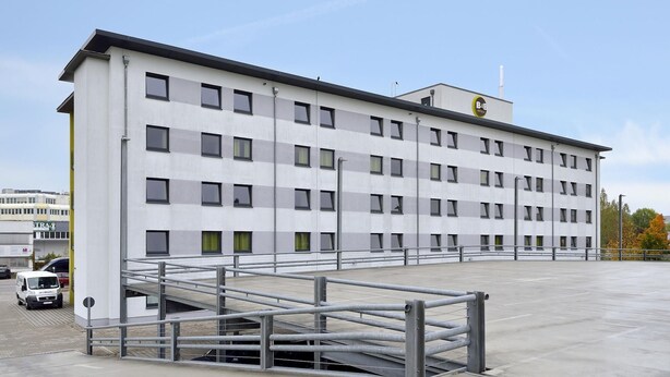 Un edificio moderno con tejado plano, múltiples ventanas y entrada con portón.