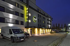 En moderne hotelbygning med et skilt der viser "B&B Hotels" og en parkeringsplads med flere biler.