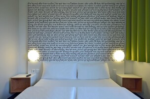 A neatly made bed with white linens, two bedside tables, and a wall-mounted light fixture.