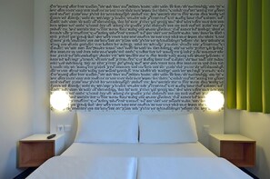 A neatly made bed with white linens, two bedside tables, and a wall-mounted light fixture. - B&B Hotel München Messe Dornach (Aschheim)