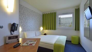 Habitación de hotel con una cama, un escritorio con un control remoto, una revista, un teléfono en la pared y un televisor.