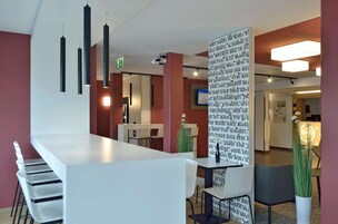 Un moderno vestíbulo de hotel con un mostrador de recepción blanco, lámparas colgantes negras y una pared grande con texto.