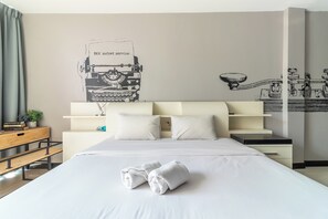 A hotel room with a neatly made bed, a desk with a lamp, a shelf with books and a plant, and a wall with a mechanical drawing. - The Secret Service Hotel (Bangkok)