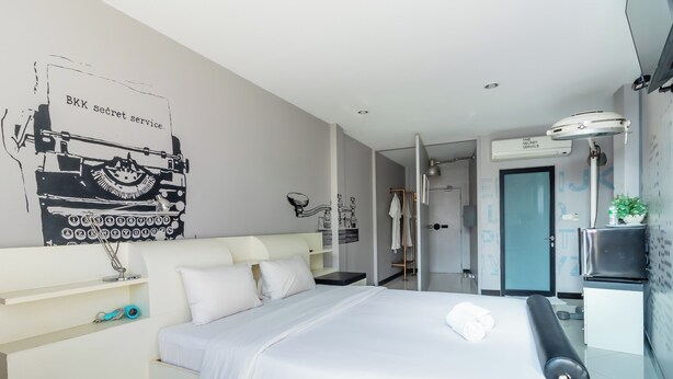 A modern hotel room with a bed, a desk, a chair, a TV, and a bathroom visible through an open door. - The Secret Service Hotel (Bangkok)