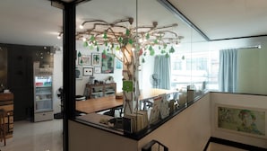 A modern interior with a glass partition, a wooden desk, and a decorative tree with hanging lights. - The Secret Service Hotel (Bangkok)