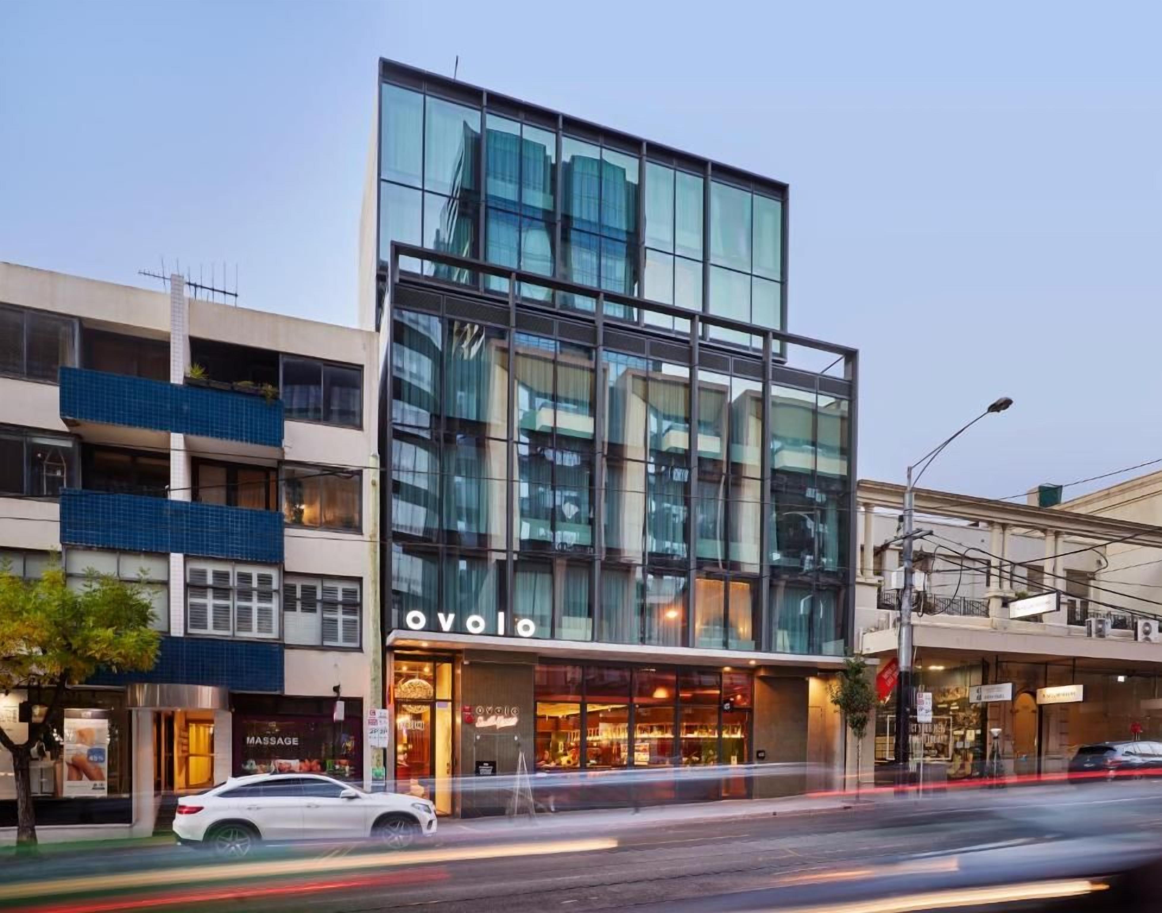 A modern building with a glass facade, a visible 'OVOLO' sign, and a 'MASSAGE' shop on the ground floor.