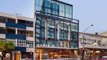 A modern building with a glass facade, a visible 'OVOLO' sign, and a 'MASSAGE' shop on the ground floor.