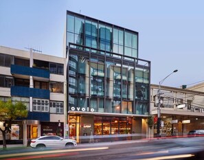 A modern building with a glass facade, a visible 'OVOLO' sign, and a 'MASSAGE' shop on the ground floor.