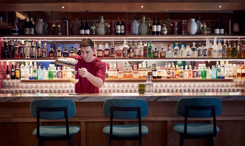 A bar with shelves of liquor bottles and a bartender preparing a drink.