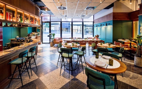 Un restaurant doté d’un bar, de nombreuses tables et chaises, et de grandes fenêtres offrant une vue sur la rue.