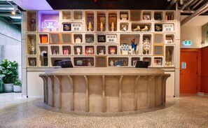 A reception desk with a modern design, surrounded by a variety of decorative items and shelves. - Ovolo Melbourne South Yarra a Wyndham Hotel (Melbourne)