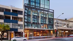Een modern gebouw met een glazen gevel, een goed zichtbaar 'OVOLO' bord en een 'MASSAGE' winkel op de begane grond.
