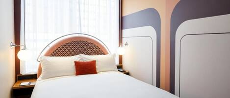 Ein ordentlich bezogenes Bett mit einem gemusterten Kopfteil, einer Nachttischlampe und einer Zeitschrift auf dem Bett.