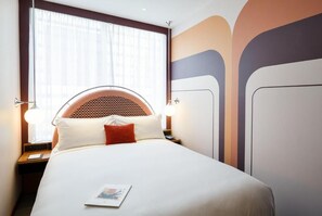 Ein ordentlich bezogenes Bett mit einem gemusterten Kopfteil, einer Nachttischlampe und einer Zeitschrift auf dem Bett.